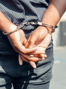 Rear view of a person in handcuffs outdoors, symbolizing law enforcement and justice.